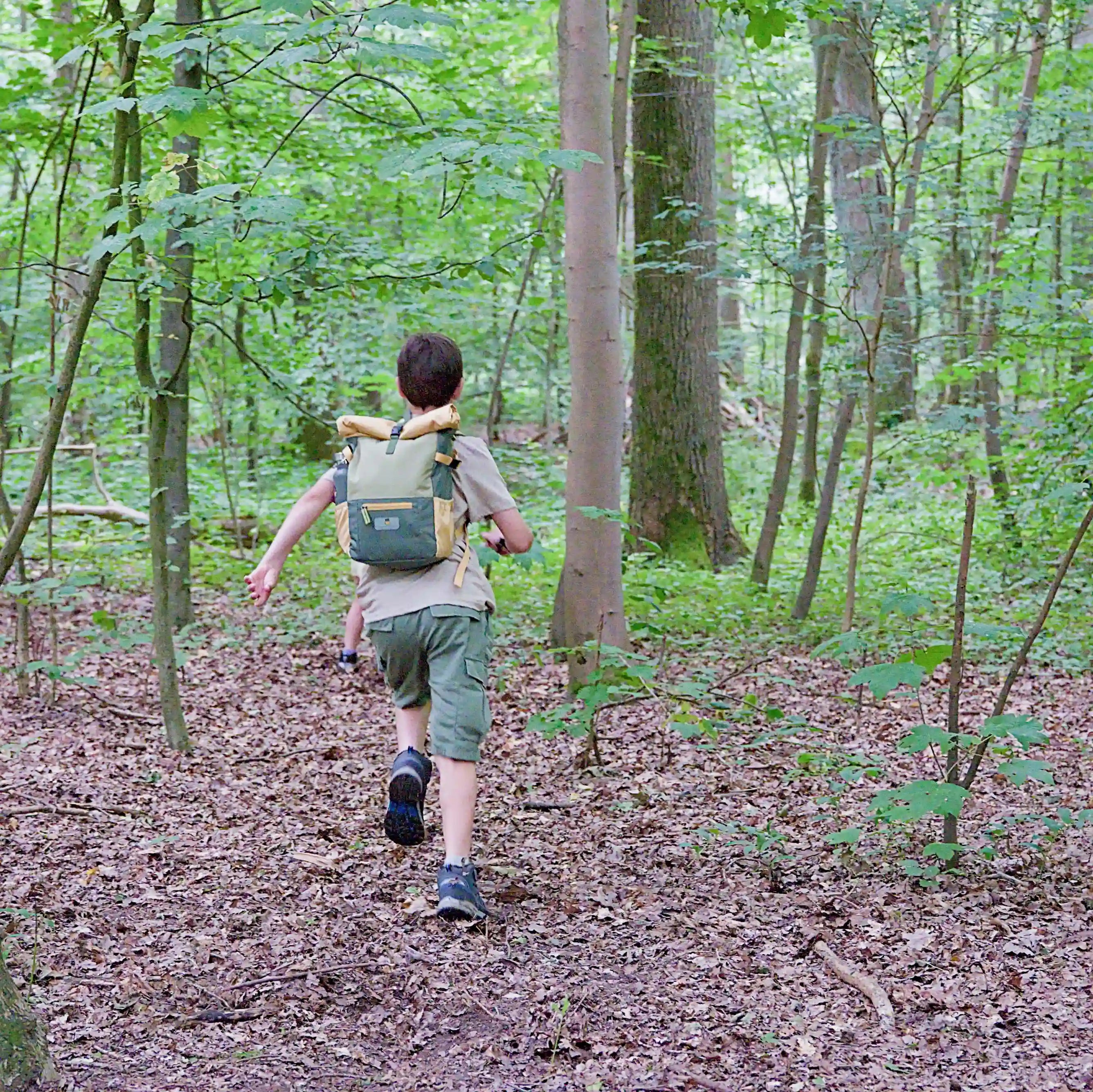 Kid running in the woods with sustainable recycled polyester rolltop backpack from the collection MAJU in green and orange - The Melon Explorer