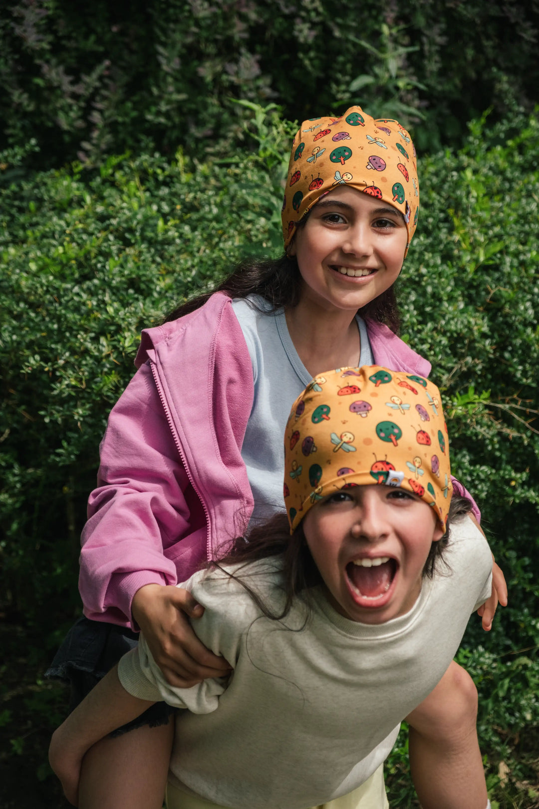 Two children wearing Woods organic cotton beanies during a piggyback ride
