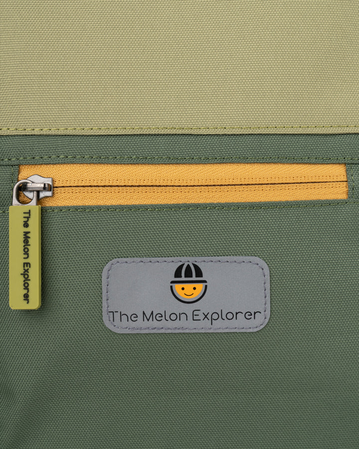 Detail of the front pocket of the sustainable recycled polyester rolltop backpack from the MAJU collection for children in green and orange – The Melon Explorer