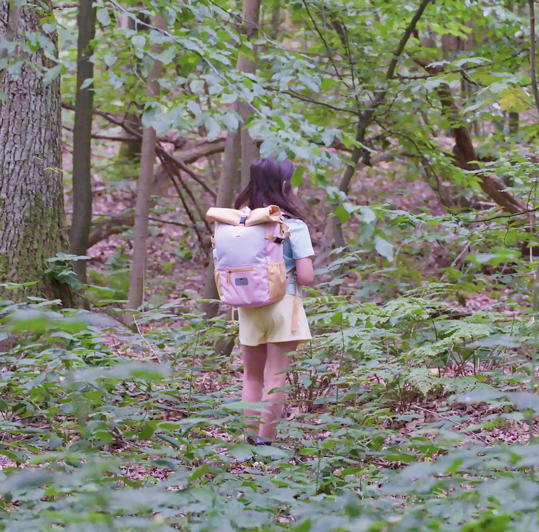 Girl in the forest with the recycled rolltop backpack from the Maju collection in pink/purple/orange