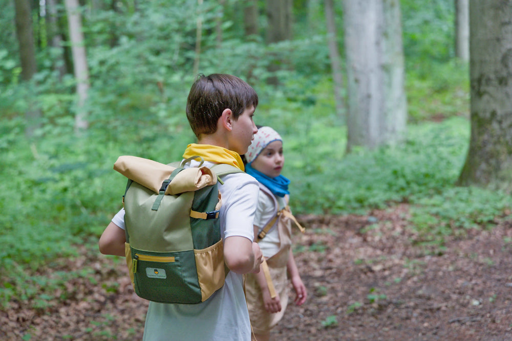 Boy in the forest with the recycled rolltop backpack form the Maju collection in green/orange