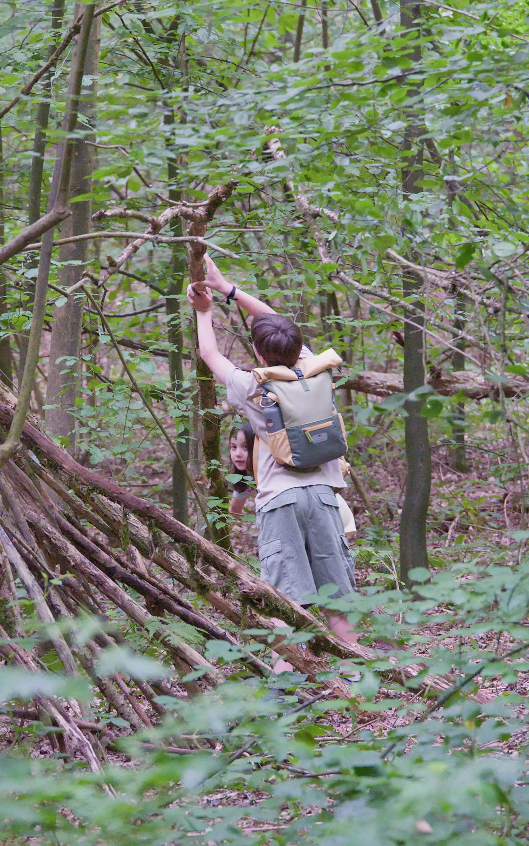 Boy building a shelter with the recycled rolltop backpack form the Maju collection in green/orange
