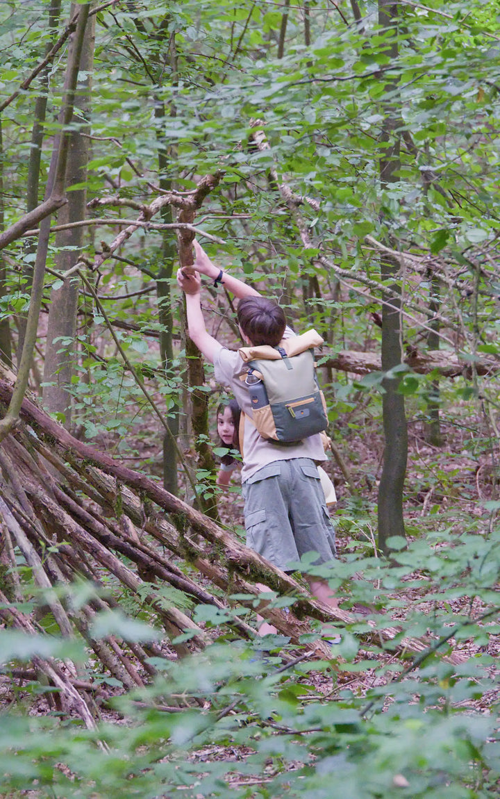 Boy building a shelter with the recycled rolltop backpack form the Maju collection in green/orange