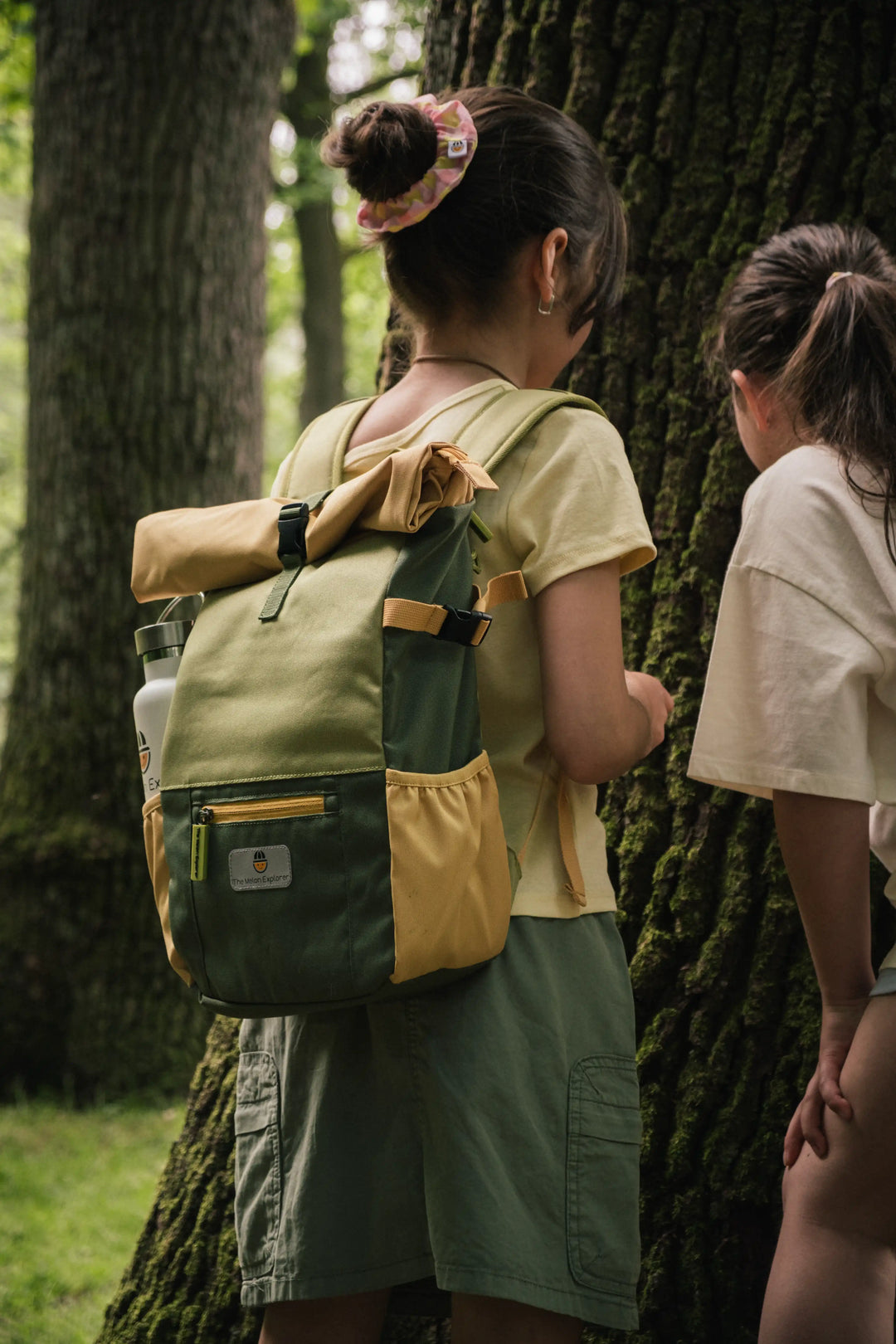 Two girls wearing Maju recycled polyester backpacks exploring a tree trunk